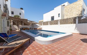 Une piscine dotée d’une terrasse carrelée, de chaises longues et d’un mur en pierre.