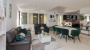 A modern living room with a leather sofa, a glass coffee table, and a dining area with green chairs. - Family Dream Dalmatia - Split by Villas Guide (Košute)
