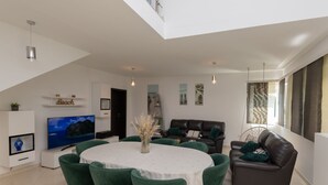 A modern living room with a TV, green chairs, a dining table, and a sofa. - Family Dream Dalmatia - Split by Villas Guide (Košute)