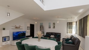 A modern living room with a TV, green chairs, a dining table, and a sofa.