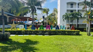 A sign with the words "PLAYYABLANCA" in colorful letters, surrounded by well-maintained grass and palm trees, with a building in the background.