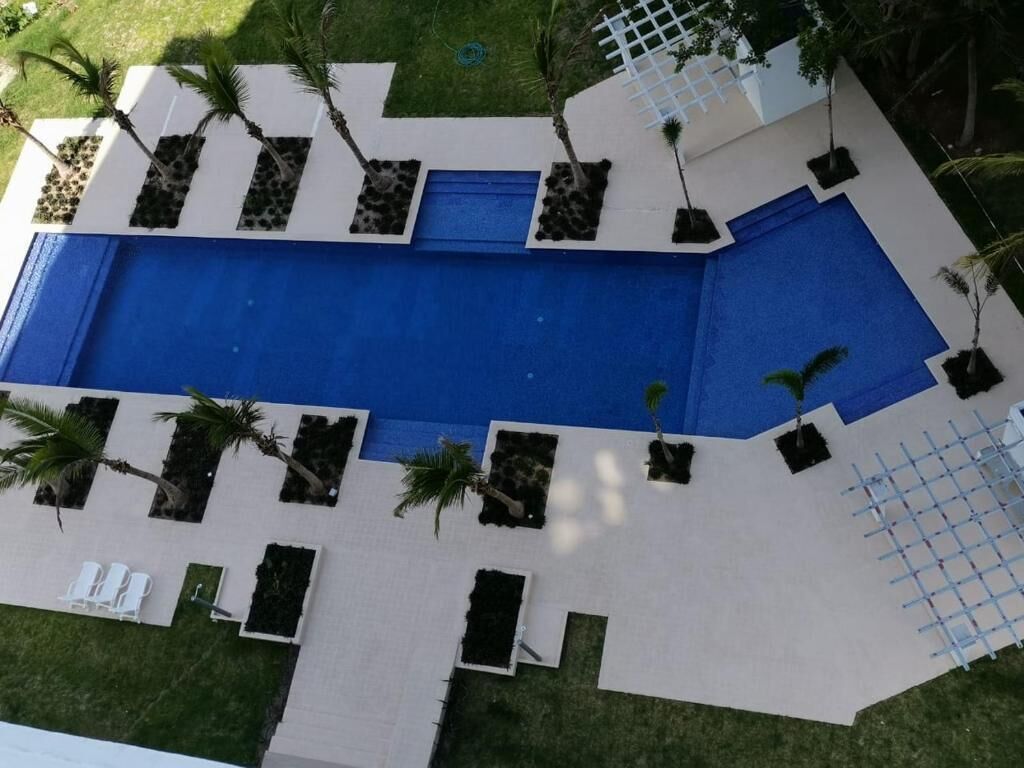 Une piscine dotée d’une plage bleue, entourée de plantes en pot et d’une clôture blanche.