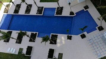 Une piscine dotée d’une plage bleue, entourée de plantes en pot et d’une clôture blanche.