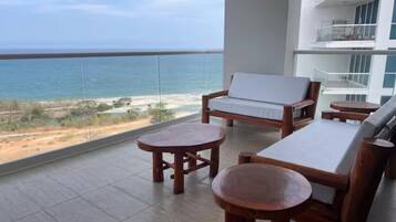 Een balkon met uitzicht op de oceaan, houten meubels en een witte stoel met kussens.