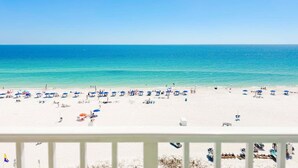 A beach with white sand, clear blue water, and umbrellas.
