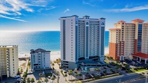 A hotel with multiple floors, a parking lot, and a view of the ocean.