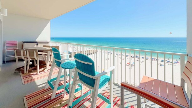 A balcony with a view of the beach, a table with chairs, and a small seating area.