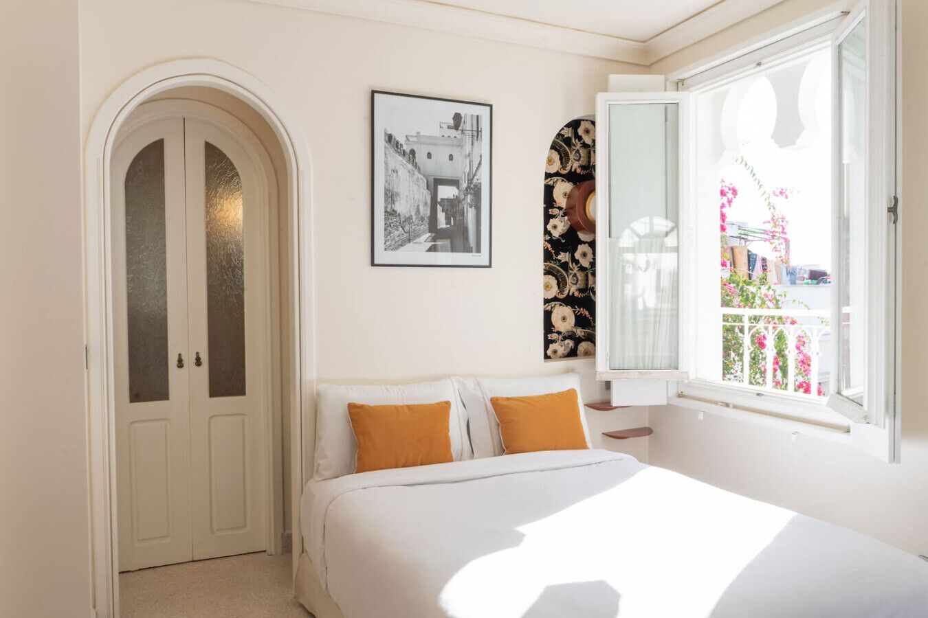 Une chambre à coucher comprenant un lit, deux oreillers, un tableau encadré, un panneau décoratif mural et une fenêtre donnant sur un balcon.