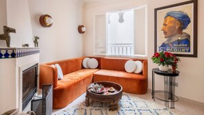 A cozy living room with a fireplace, a sofa, a coffee table, and a framed poster on the wall. - Absinthe Guesthouse : Charming Suite With Sea View - Battuta Suite (Tangier)