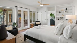 A modern bedroom with a large bed, a ceiling fan, and a view of the outdoor area.