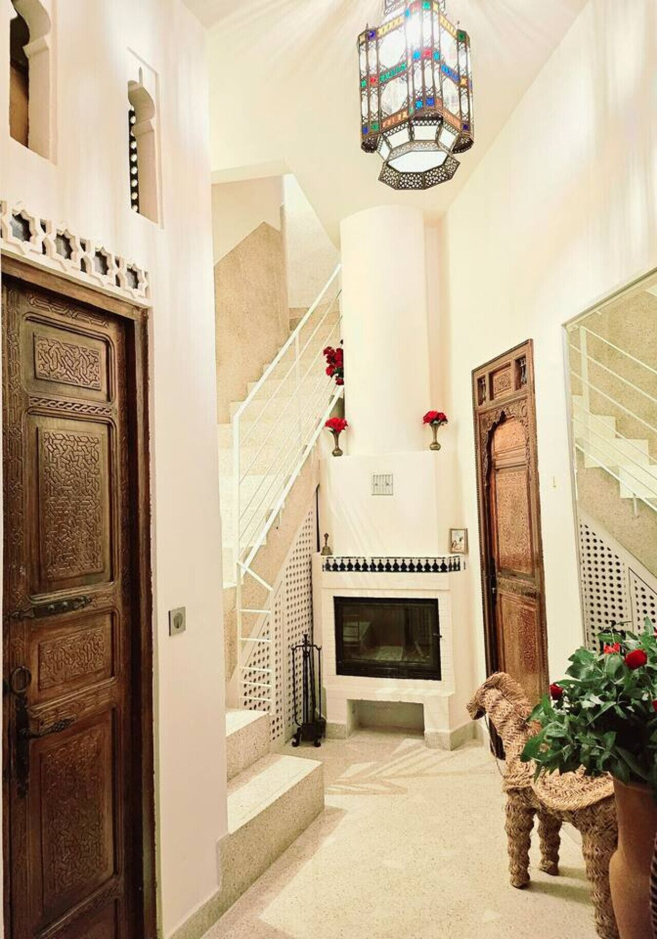 A hallway with a wooden door, a staircase, a fireplace, and a hanging light fixture.