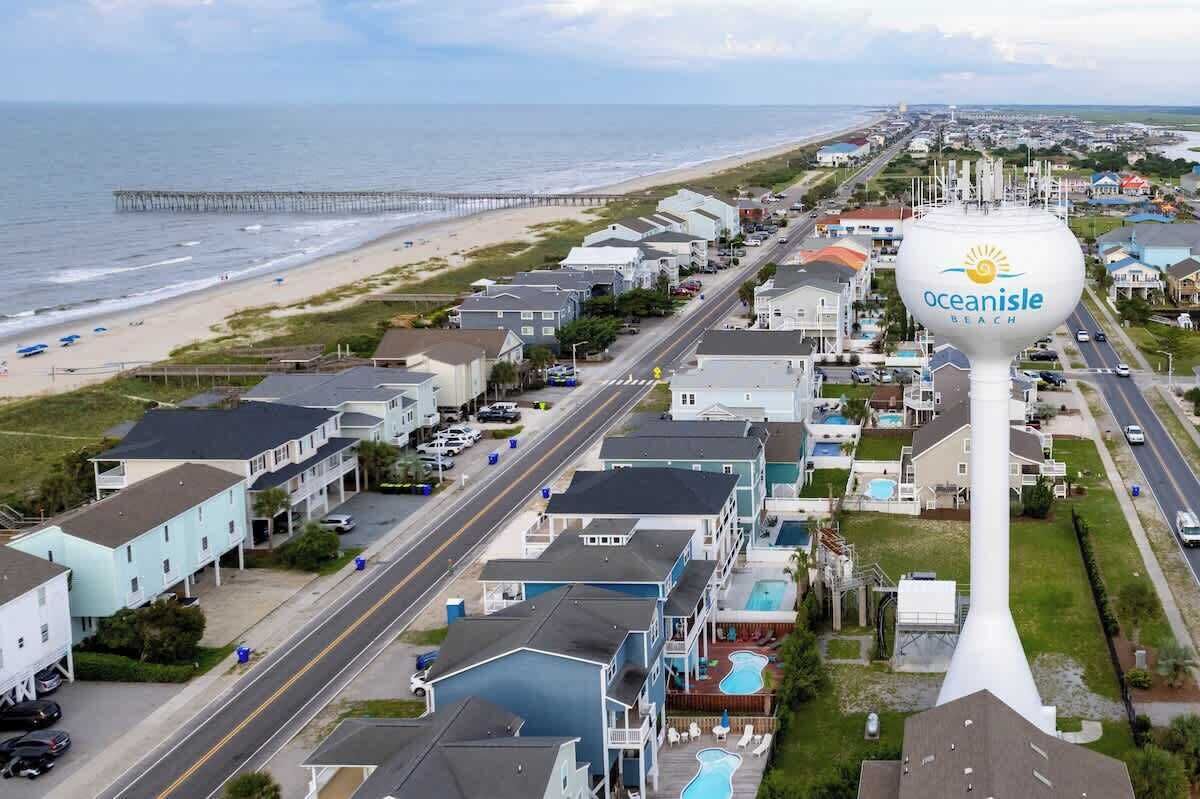 En kuststad med ett markant vattentorn som bär inskriptionen ”Oceanisle Beach”, en strand och en pir.