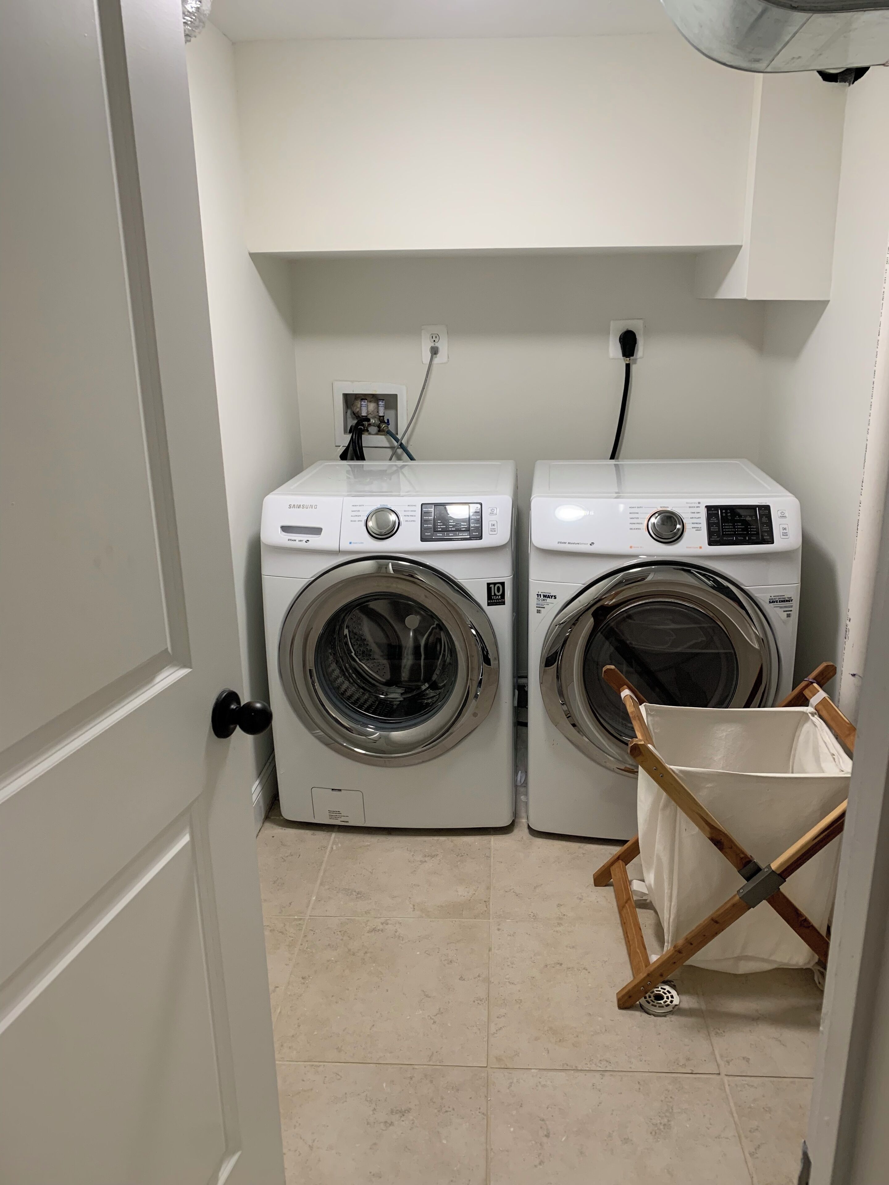 A laundry room with two front-loading washing machines, a power outlet, and a wooden folding chair.