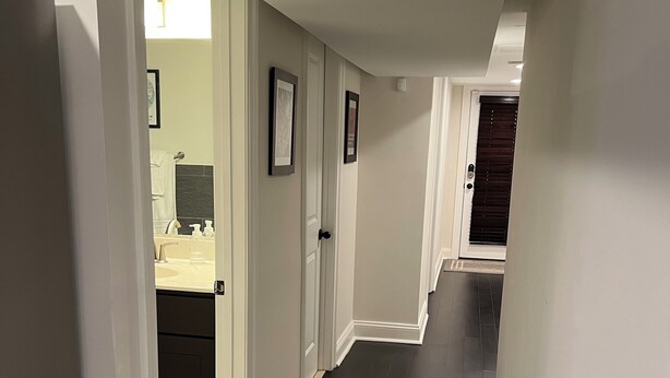 A hallway with dark wooden flooring, white walls, and a door leading to a bathroom with a sink and mirror. - Charming, modern 1-bedroom English Basement in heart of DC with WiFi, AC (Washington)