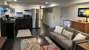 A modern kitchen with a stainless steel refrigerator, a microwave, and a stove. There is a gray sofa with white pillows and a wooden cabinet with a lamp. - Charming, modern 1-bedroom English Basement in heart of DC with WiFi, AC (Washington)