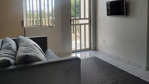 Una sala de estar con un sofá, un televisor de pantalla plana montado en la pared y un ventilador de techo.