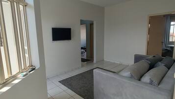 Un salón amplio con un sofá gris, un televisor de pantalla plana montado en la pared y un ventilador de techo.
