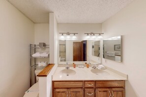 A bathroom with two sinks, a mirror, and a shelf with towels. - Lakeside Bliss (Hot Springs Village)