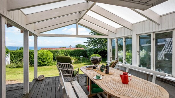 A covered outdoor area with a wooden table and chairs, a grill, and a view of the sea. - Amazing apartment in Asperup with sauna (Asperup)