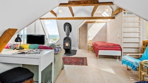 A cozy attic bedroom with a wooden ceiling, a fireplace, a desk with a computer, a bed with a red blanket, and a view of the outdoors. - Amazing apartment in Asperup with sauna (Asperup)
