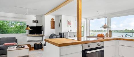A modern kitchen with a wooden countertop, white cabinetry, and a large window overlooking a body of water.