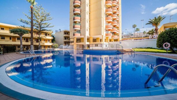 A swimming pool surrounded by a high-rise building with multiple balconies. - Cozy 2-Bed & Sofa-bed Studio in Los Cristianos (Playa de la Américas)