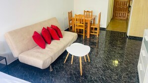 A living room with a beige sofa, red cushions, a small white table, and a wooden dining set. - Cozy 2-Bed & Sofa-bed Studio in Los Cristianos (Playa de la Américas)
