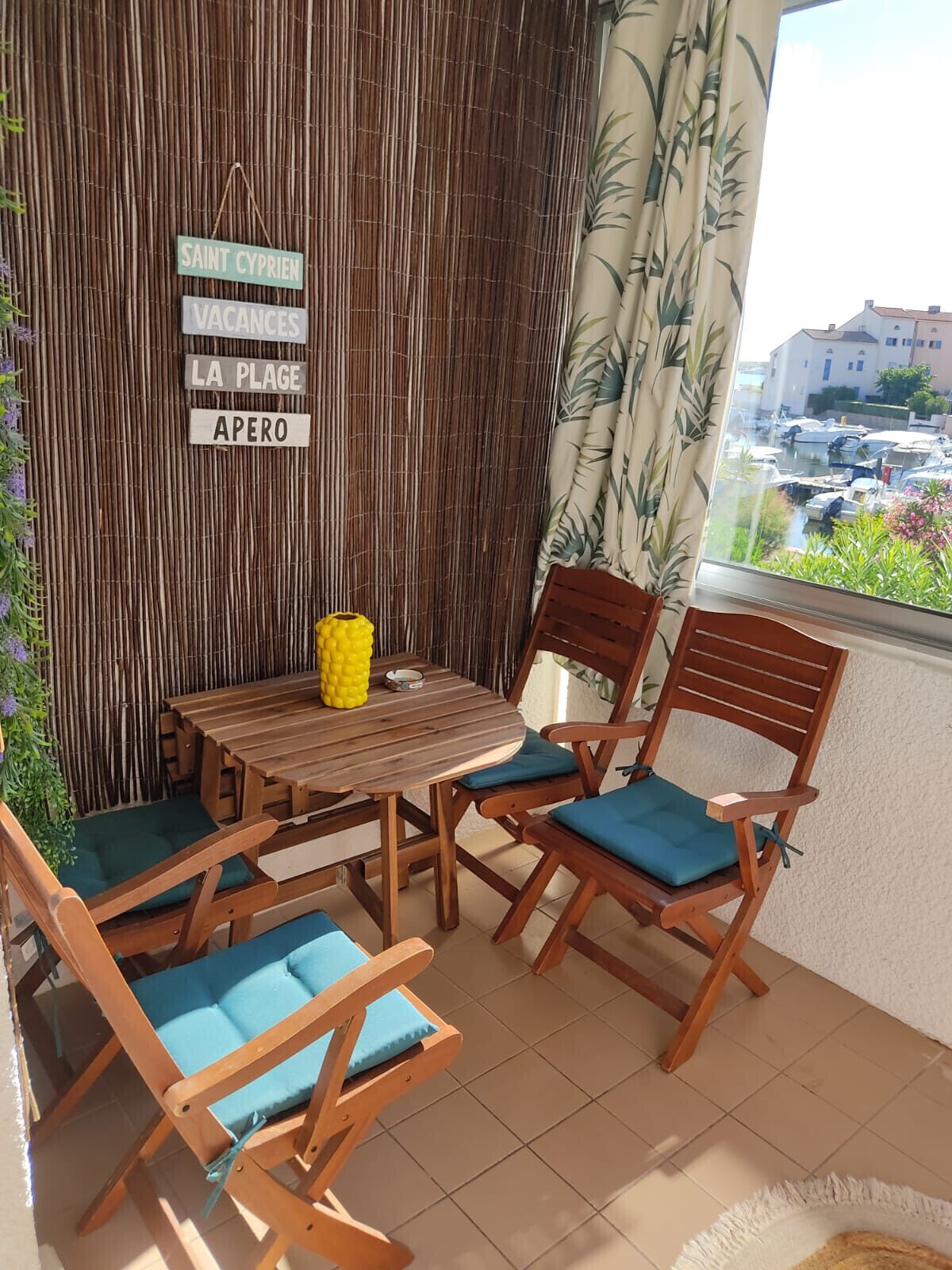 Een houten tafel en stoelen op een balkon met een bamboe muur en uitzicht op boten.