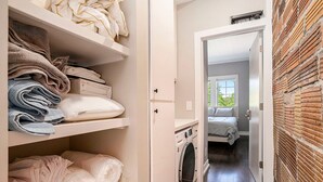 Un cuarto de lavado con toallas ordenadas en estantes, una lavadora y una cama en la habitación contigua.