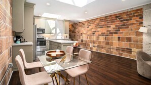 Una cocina moderna con tragaluz, un comedor con mesa y sillas de vidrio, y una pared de ladrillo.