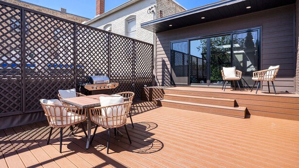 Un patio exterior con cubierta de madera, mobiliario de mimbre y una parrilla.