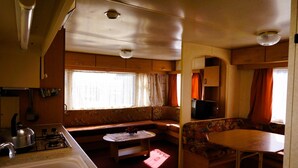 Ein kompaktes Wohnmobil-Interieur mit Küchenzeile, einer Sitzecke mit Tisch und Bank sowie einem kleinen Fenster für natürliches Licht.