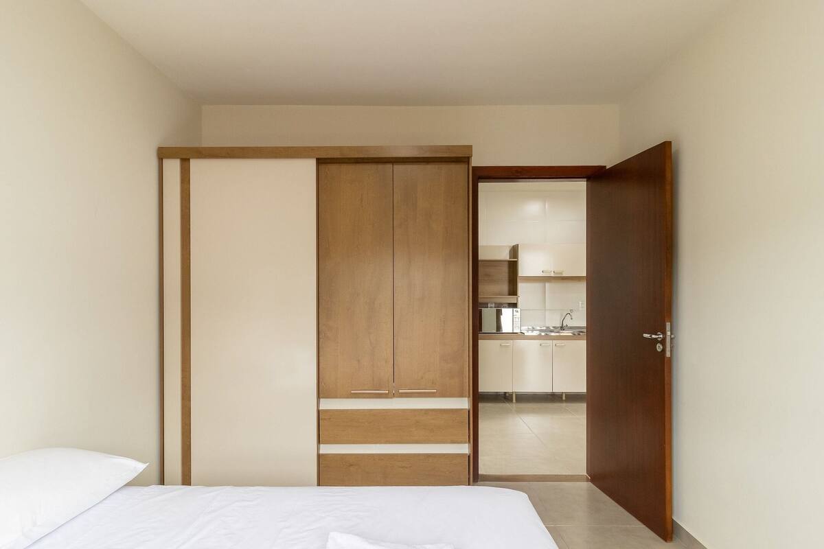 Ein Schlafzimmer mit Bett, Kleiderschrank und Blick in eine Küchenzeile.