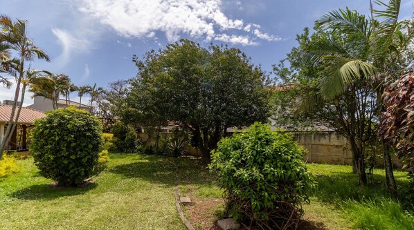 A well-maintained garden with various trees and shrubs, a stone wall, and a clear sky. - SJS - Condominium Near the Beach of the English (Florianópolis)
