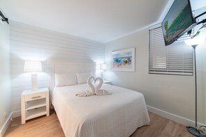 A neatly arranged bedroom with a bed, bedside tables, a wall-mounted TV, and a framed picture.