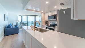 A modern kitchen with a large island, stainless steel appliances, and a view to the outside.