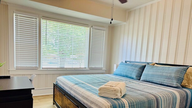 Un dormitorio con cama, escritorio y ventanas con persianas.