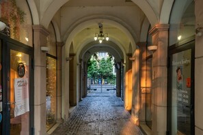 A corridor with arched ceilings and a cobblestone floor, leading to a gated entrance.