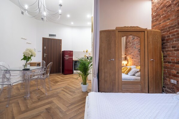 A modern hotel room with a wooden wardrobe, a dining area with a glass table and chairs, and a brick wall.
