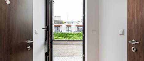 A doorway leading to a balcony with a view of buildings and greenery.