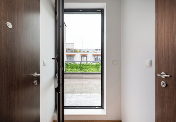 A doorway leading to a balcony with a view of buildings and greenery.