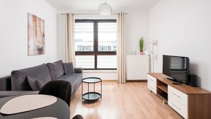 Ett modernt vardagsrum med en grå soffa, ett runt soffbord, en tv på ett träställ och ett fönster med gardiner.