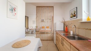 Una cocina compacta con un separador de madera, un lavamanos y un comedor visible a través del tabique.