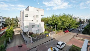 Un edificio moderno con techo plano y amplios ventanales, rodeado de una zona pavimentada y automóviles estacionados.