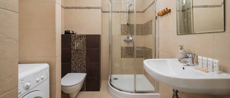 A modern bathroom with a glass shower enclosure, a built-in washing machine, and a sink with toiletries.