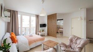 Una habitación de hotel moderna con cama, una mesita de madera, un sofá, televisor y una zona de cocina.