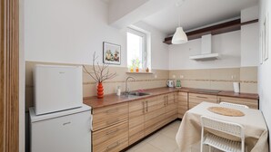 Una cocina moderna con armarios de madera, un refrigerador blanco, un lavamanos y una zona de comedor con mesa y silla.