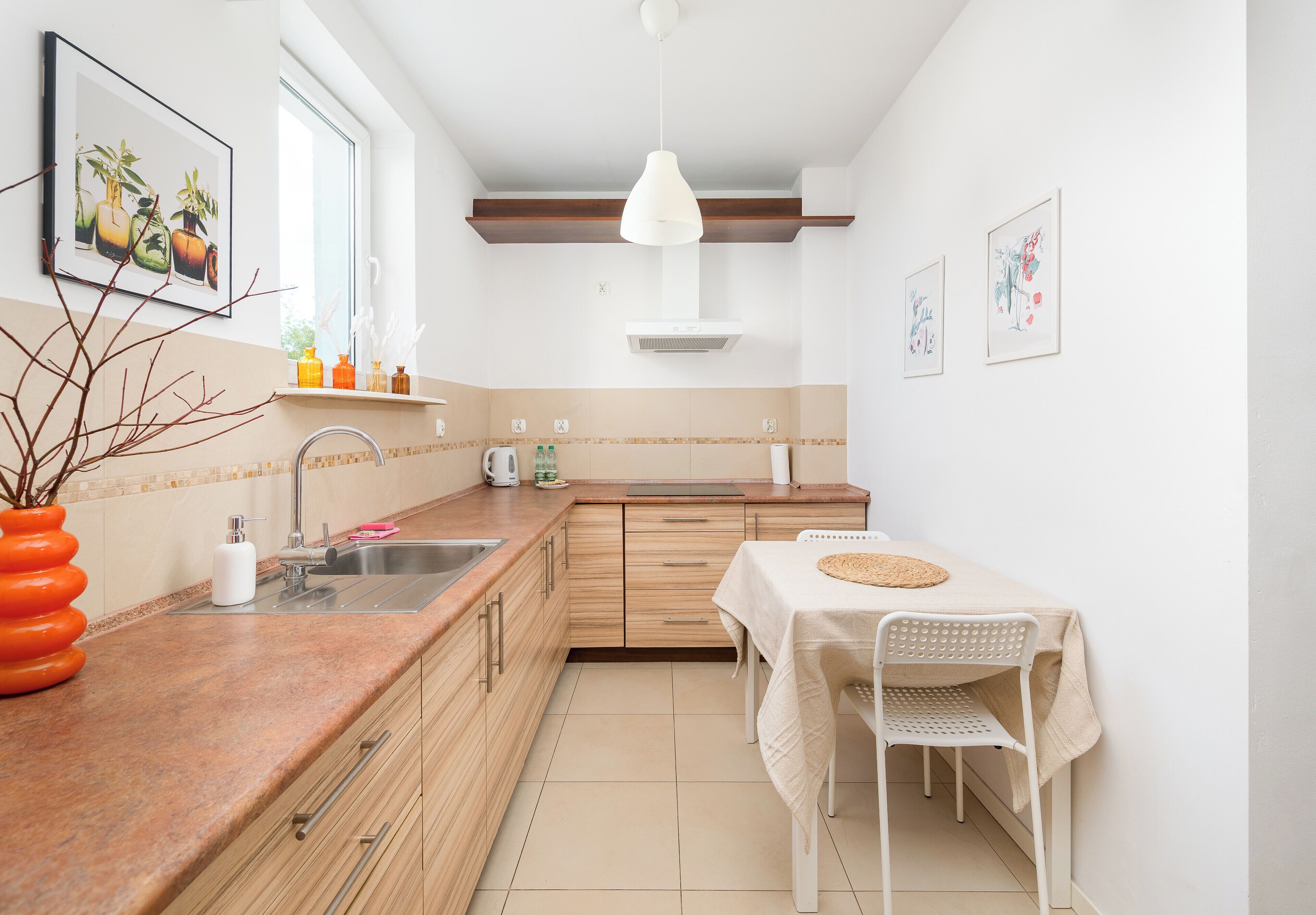 Una cocina moderna con armarios de madera, un lavamanos, una mesa de comedor con sillas y obras de arte en las paredes.