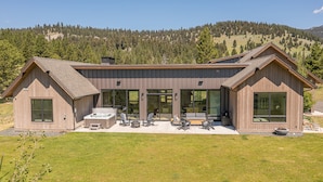 Ein modernes, zweistöckiges Haus mit einer großen Terrasse, großen Fenstern und Blick auf einen bewaldeten Hügel.
