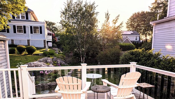 Une terrasse en bois avec deux fauteuils Adirondack et une petite table ronde, le tout entouré d’une balustrade blanche.